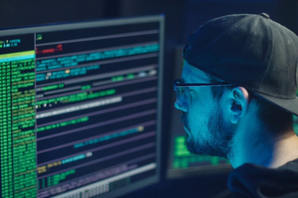 pexels-photo-6963098 A cybersecurity expert inspecting lines of code on multiple monitors in a dimly lit office.